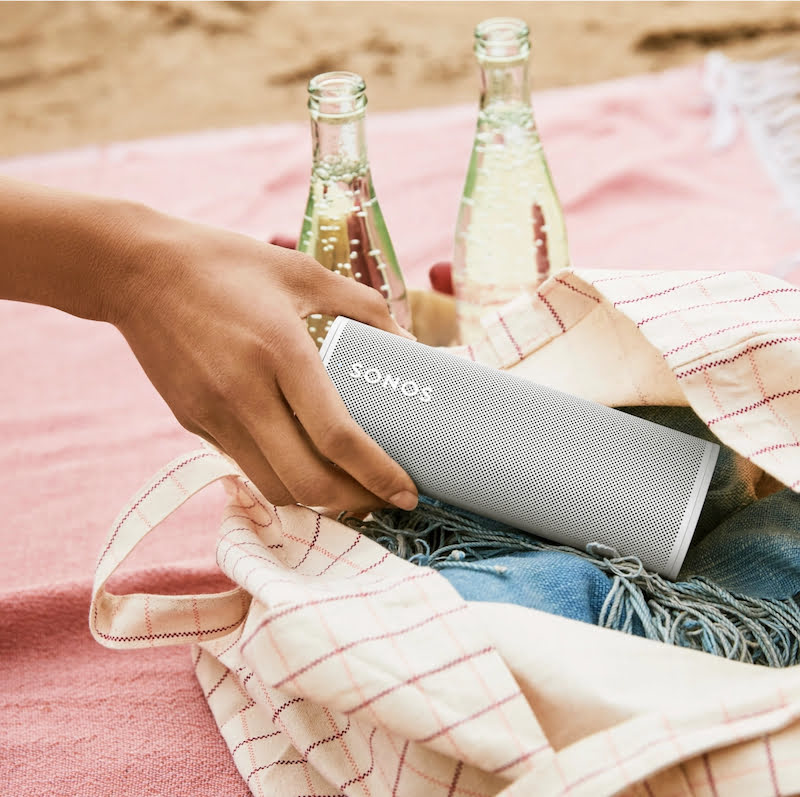 Sonos Roam wordt uit een tas gehaald op een picknickkleed met op de achtergrond twee flessen bubbels.